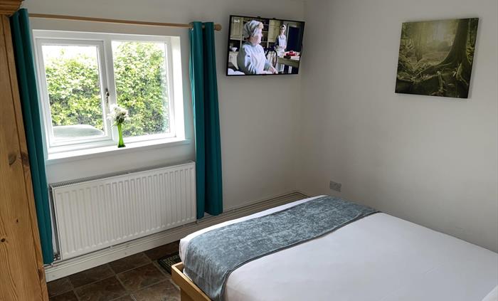 Main bedroom showing king size bed, pine wardrobe, window overlooking the private garden with blackout curtains and a 43 inch Smart TV with Freeview c